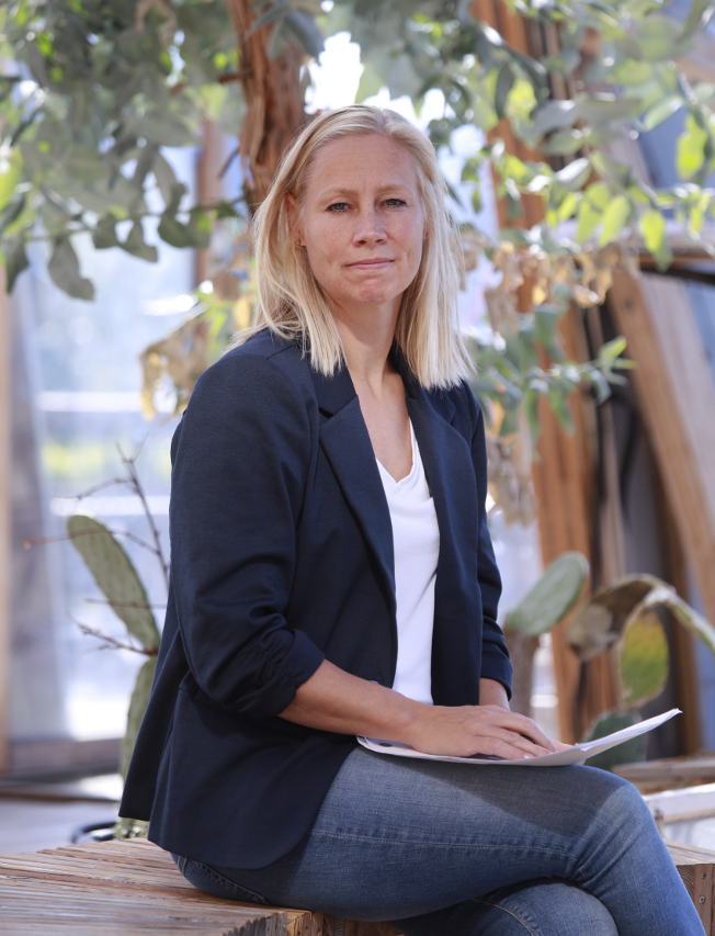 Ergoterapeut Anja Larsen sidder på en bænk under et træ med arbejdspapir i hånden